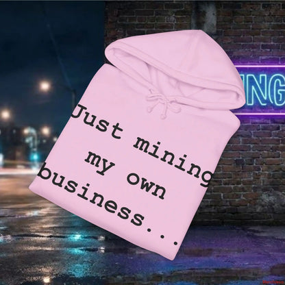 Pink hoodie with text 'Just mining my own business' against a nighttime city street background.