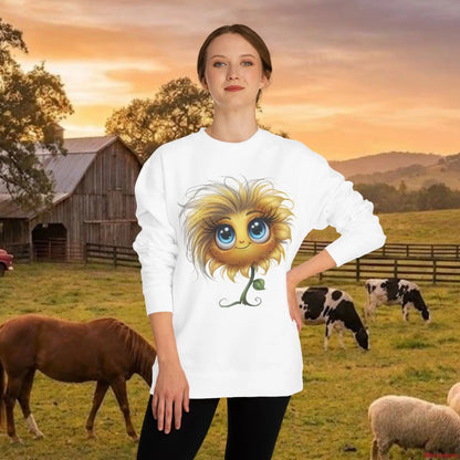 A woman wearing a white lightweight sweatshirt featuring a stylized "Sunflower with Attitude" graphic with large blue eyes and a smirk. She is standing in a rural farm setting with a wooden barn, cows, and a horse in the background during sunset